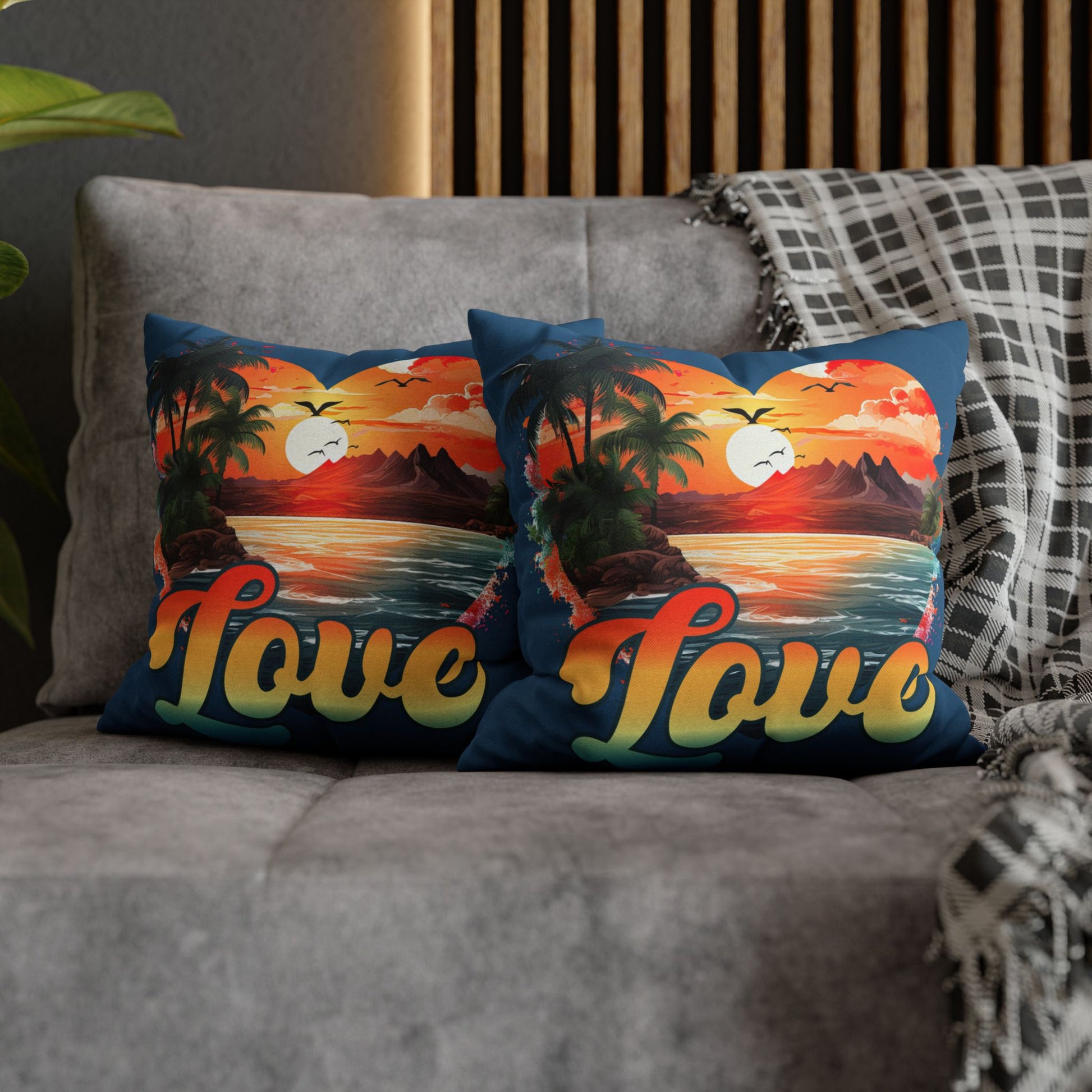 Two decorative 14" x 14" blue pillows with a sunset heart design and 'love' text on a gray couch.