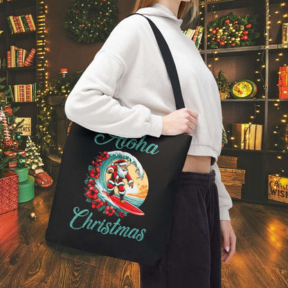 Person holding a black tote bag with 'Aloha Christmas' design in a festive setting.