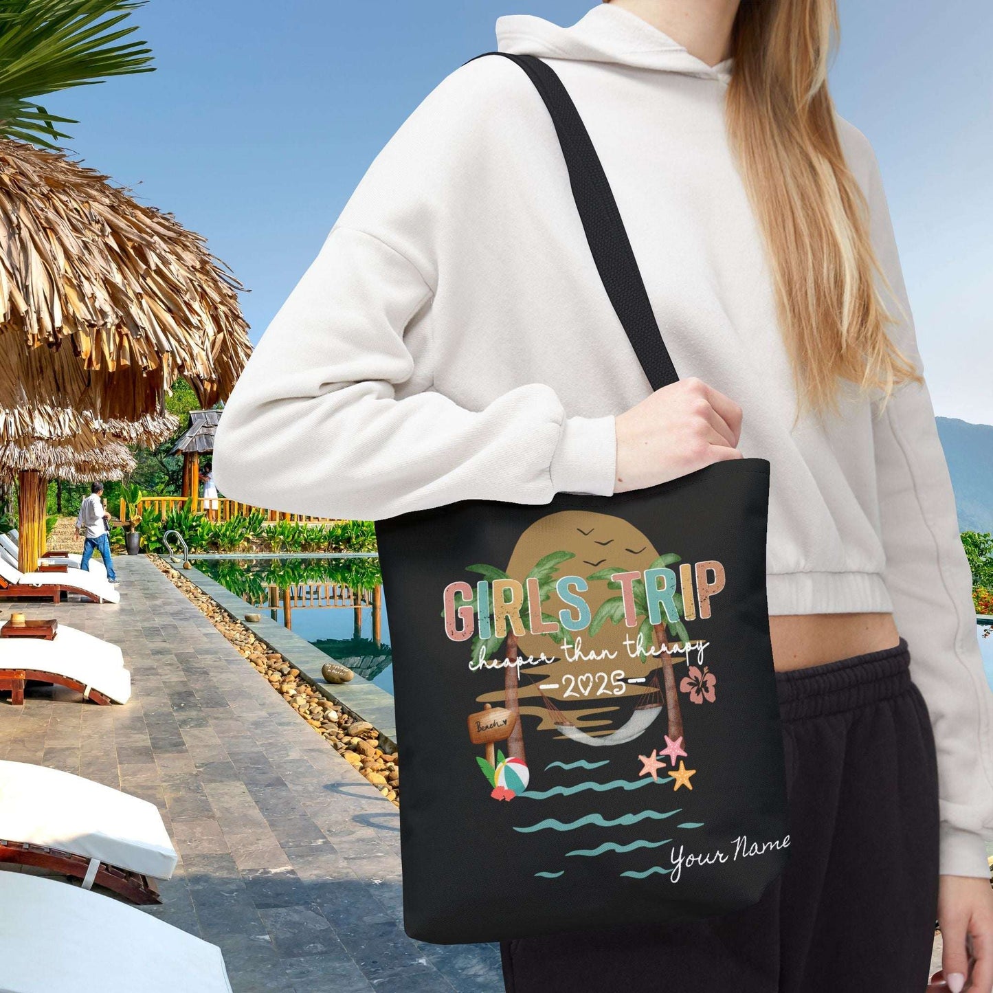 Person holding a 13" x 13" black tote bag with 'Girls Trip' beach design that can be personalized.