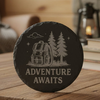 Engraved black 4" slate coaster with backpack and trees design and 'Adventure Awaits' text.