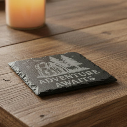 4" Black slate coaster engraved with trees and backpack with text Adventure Awaits.