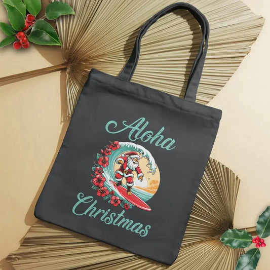 Our black tote bag with Santa surfing a curl wave with red hibiscus flowers along the wave with a sunset behind him with the text Aloha Christmas.