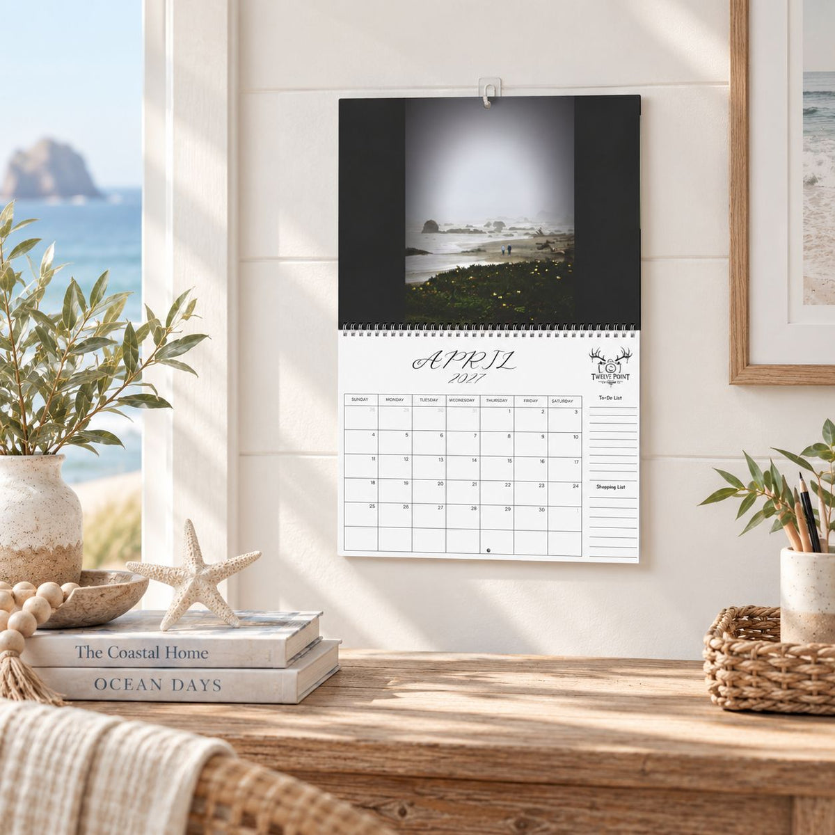 A wall-mounted April 2027 wall calendar monthly planning grid with to-do list and shopping list featuring Twelve Point Pics photography.