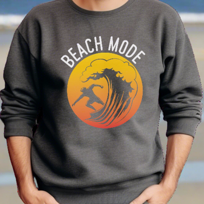 A man standing on the beach in a dark heather crewneck sweatshirt with a Person surfing a wave with a yellow and orange sunset background that says Beach Mode.