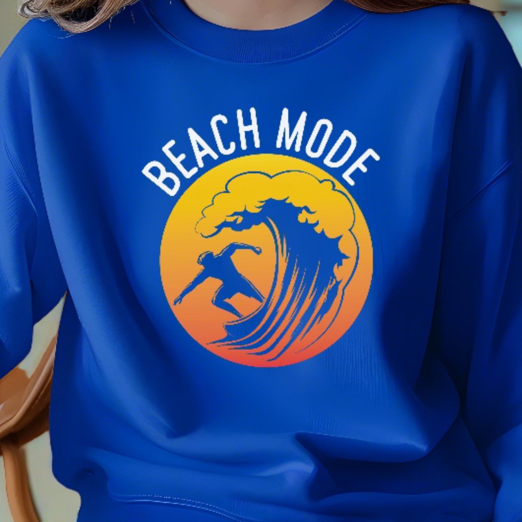 A woman sitting in a royal blue crewneck sweatshirt with a Person surfing a wave with a yellow and orange sunset background that says Beach Mode.