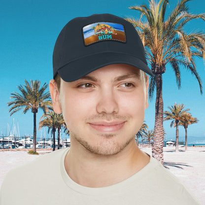 Man in navy hat with leather patch that says beach bum with a beach van, surfboards, palm trees and sun.