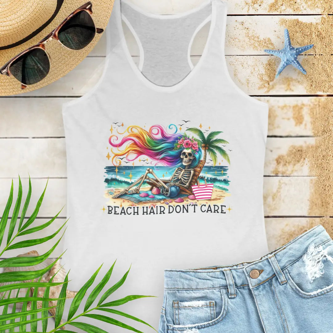 White  Racerback Tank Top with a skeleton with rainbow hair flowing in the wind laying on a beach chair at the ocean that says Beach Hair Don't Care.