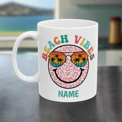 White 11 oz ceramic mug with "Beach Vibes" colorful text, featuring a retro smiley face wearing sunset sunglasses with palm trees. Personalized with a name, this coastal-themed coffee mug is perfect for beach lovers and summer vibes.text.