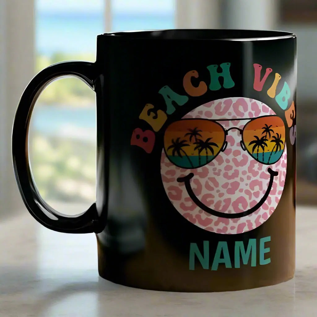 Black 11 oz ceramic mug with "Beach Vibes" colorful text, featuring a retro smiley face wearing sunset sunglasses with palm trees. Personalized with a name, this coastal-themed coffee mug is perfect for beach lovers and summer vibes.