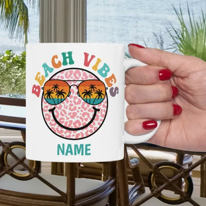 White 11 oz ceramic mug with "Beach Vibes" colorful text, featuring a retro smiley face wearing sunset sunglasses with palm trees. Personalized with a name, this coastal-themed coffee mug is perfect for beach lovers and summer vibes.