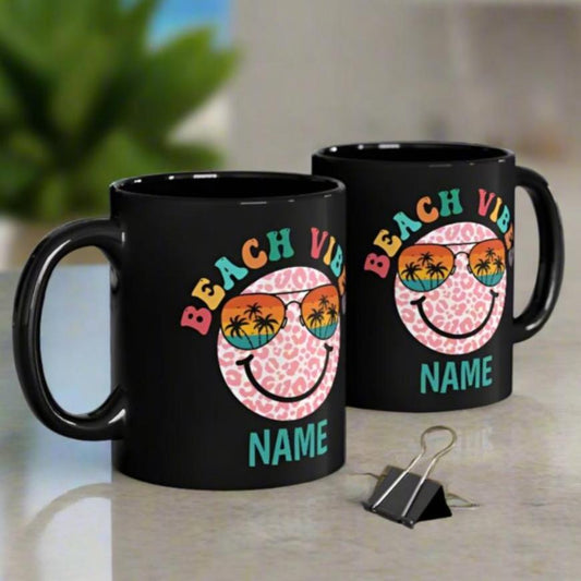 Two Black 11 oz mug that says Beach Vibes in retro text a smiley face wearing rainbow glasses and personalized with name.