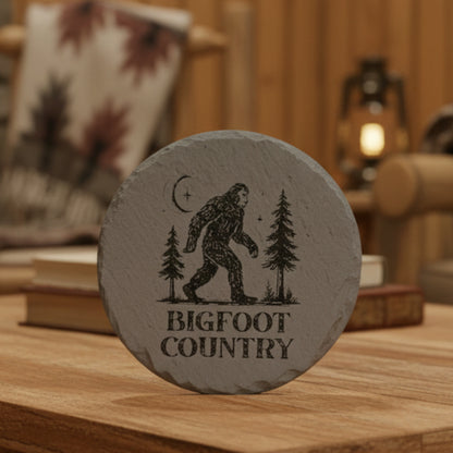 Round stone with Bigfoot design and 'Bigfoot Country' text on a wooden surface.