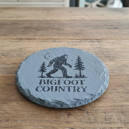 Round slate coaster with Bigfoot design and 'Bigfoot Country' text on a woven basket background.
