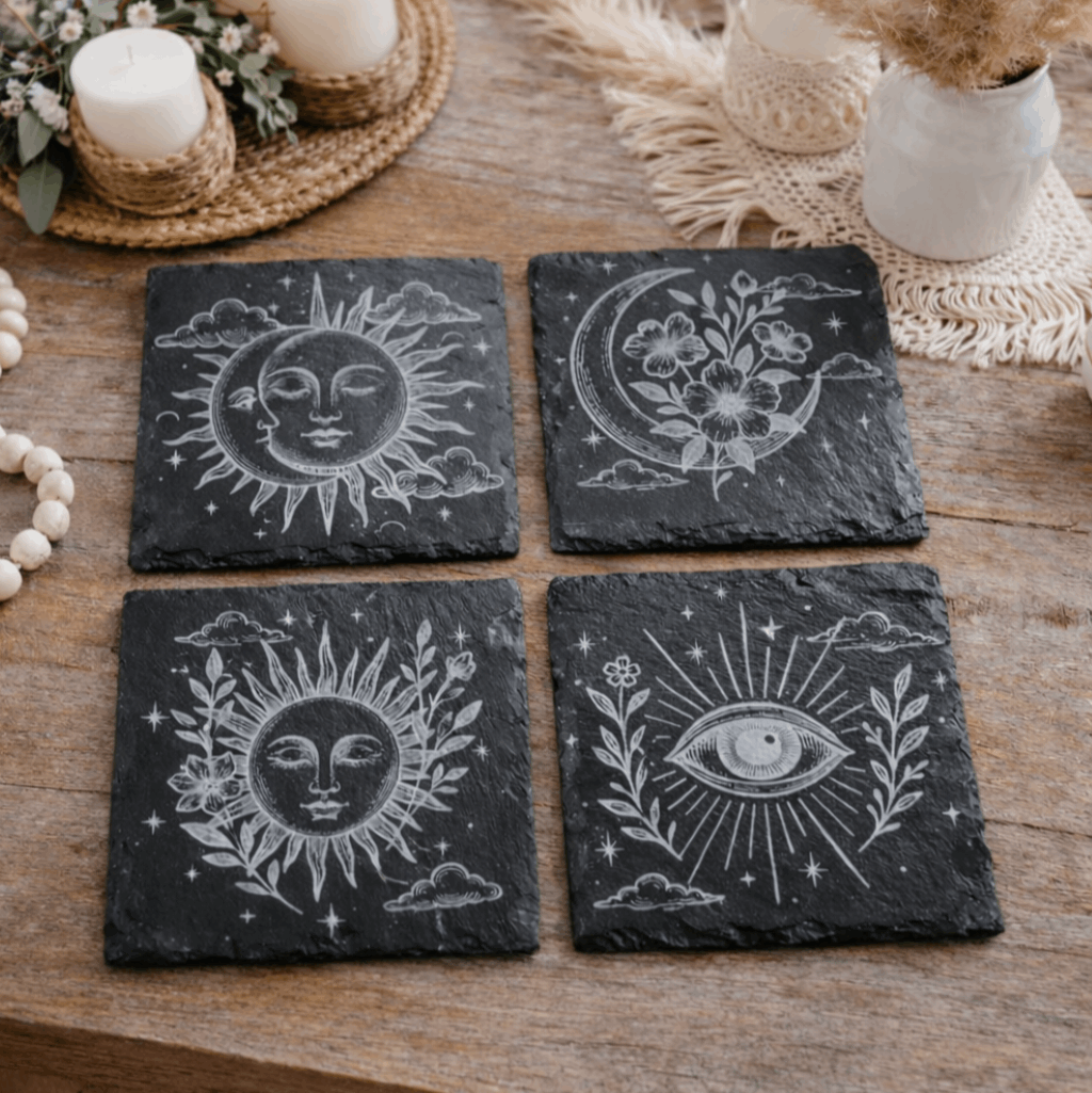 Four black slate coasters with boho celestial designs on a wooden surface.