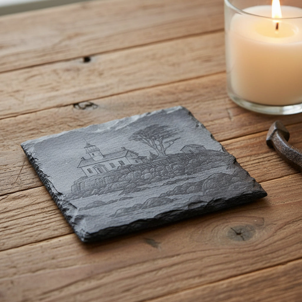 Black and white illustration of a lighthouse on a rocky shore with a tree engraved on a 4" black slate coaster.