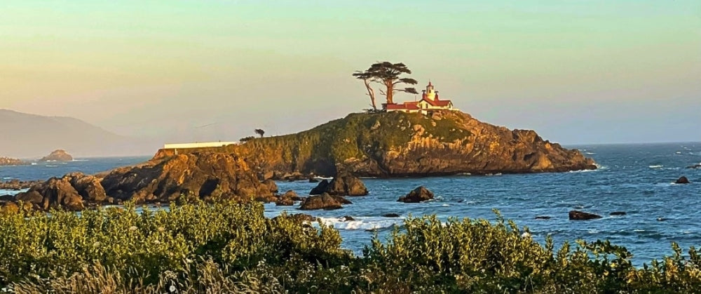 Battery Point Lighthouse on a rocky island with ocean and sunset in the background.