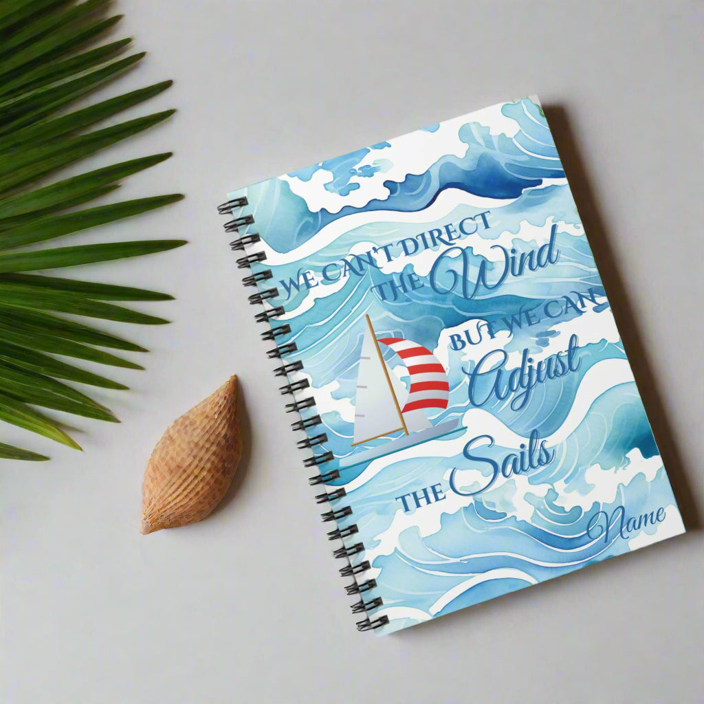 Sprial-bound notebook with waves and red and white sailboat and text We Can't Direct the Winds But We can adjust the sails.