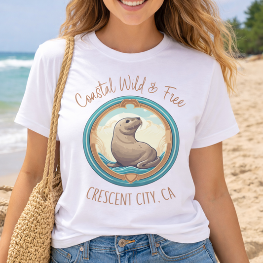 Person wearing a white t-shirt with a seal graphic and text 'Coastal Wild & Free Crescent City, CA'