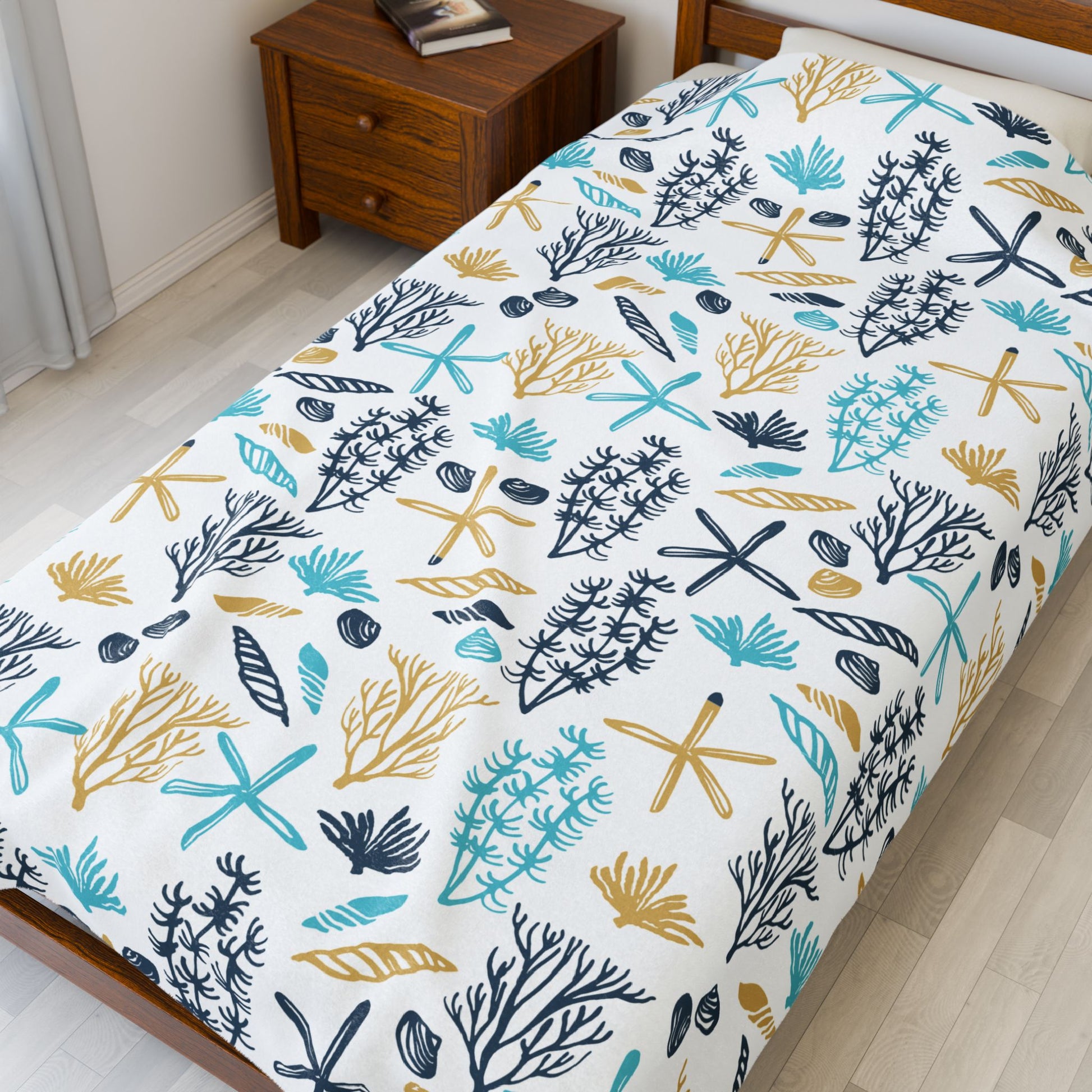 Bed with a decorative bedspread featuring a leaf pattern in blue, green, and yellow on a white background.