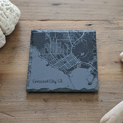 Slate coaster with engraved map of Crescent City, CA on a wooden surface.