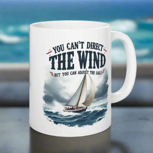 A white 11 oz. mug with a sailboat on the ocean with text 'You Can't Direct the Wind But You Can Adjust the Sails' with personalized name.