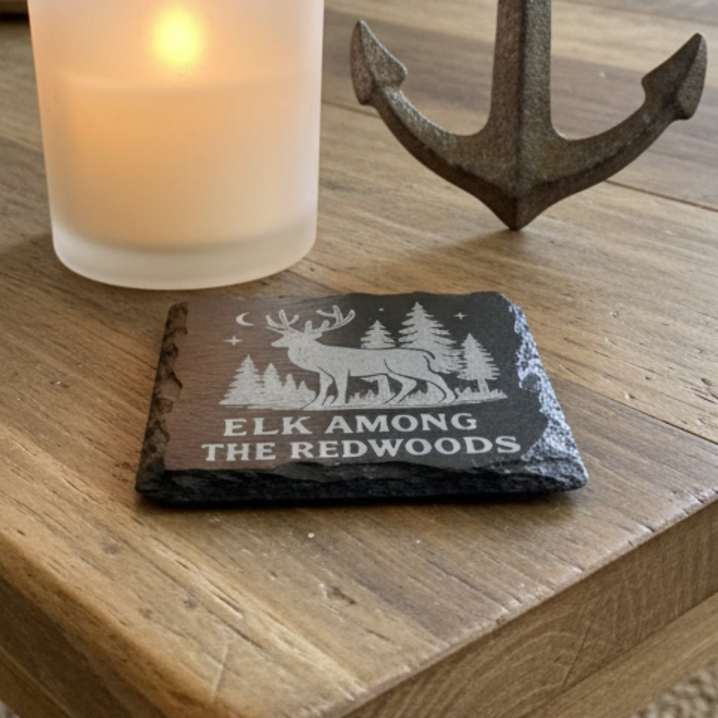 Slate coaster with engraved design of an elk and trees, text 'Elk Among the Redwoods'.