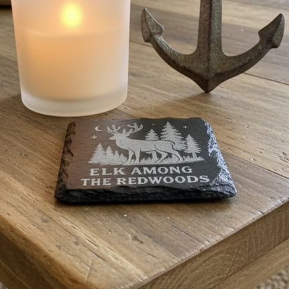 Slate coaster with engraved design of an elk and trees, text 'Elk Among the Redwoods'.