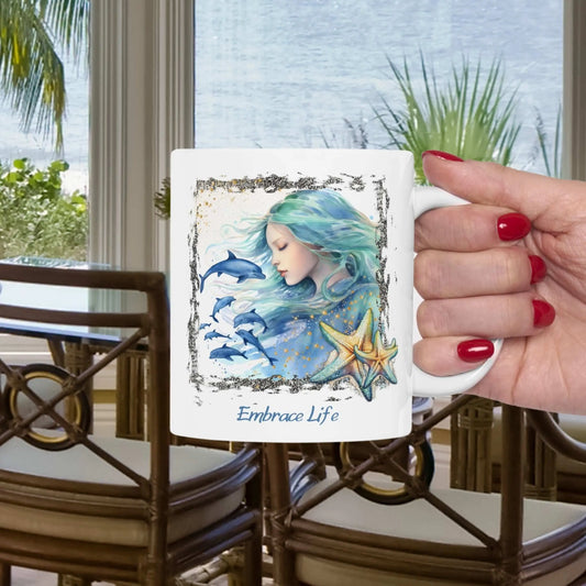 White 11 oz Ceramic Mug with a mermaid and swimming dolphins gives a mystical and positive vibe with the text Embrace Life - ideal for those who love the beach and marine life!