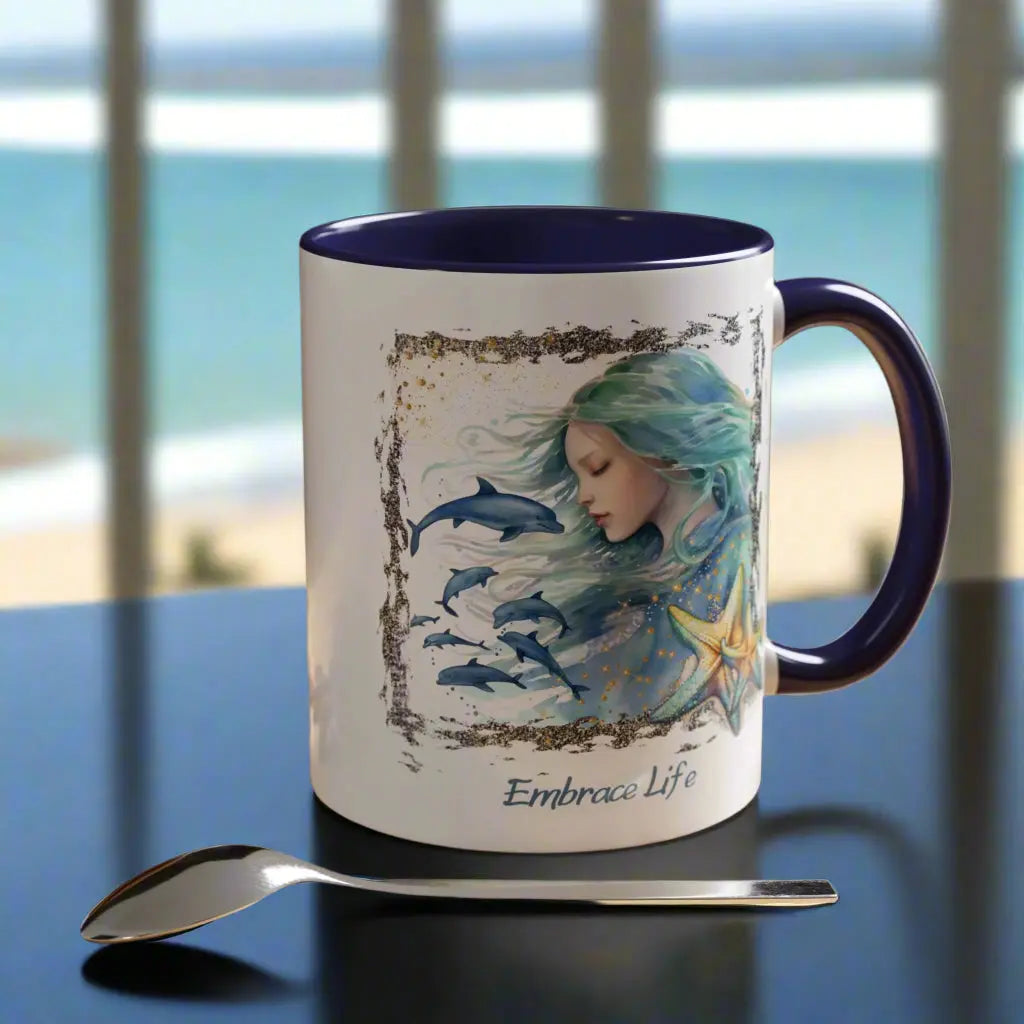 White 11 oz Ceramic Mug with blue handle and inside with a mermaid and swimming dolphins gives a mystical and positive vibe with the text Embrace Life - ideal for those who love the beach and marine life!