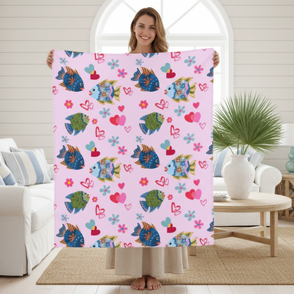 Woman holding a pink blanket with colorful fish and heart patterns in a living room.