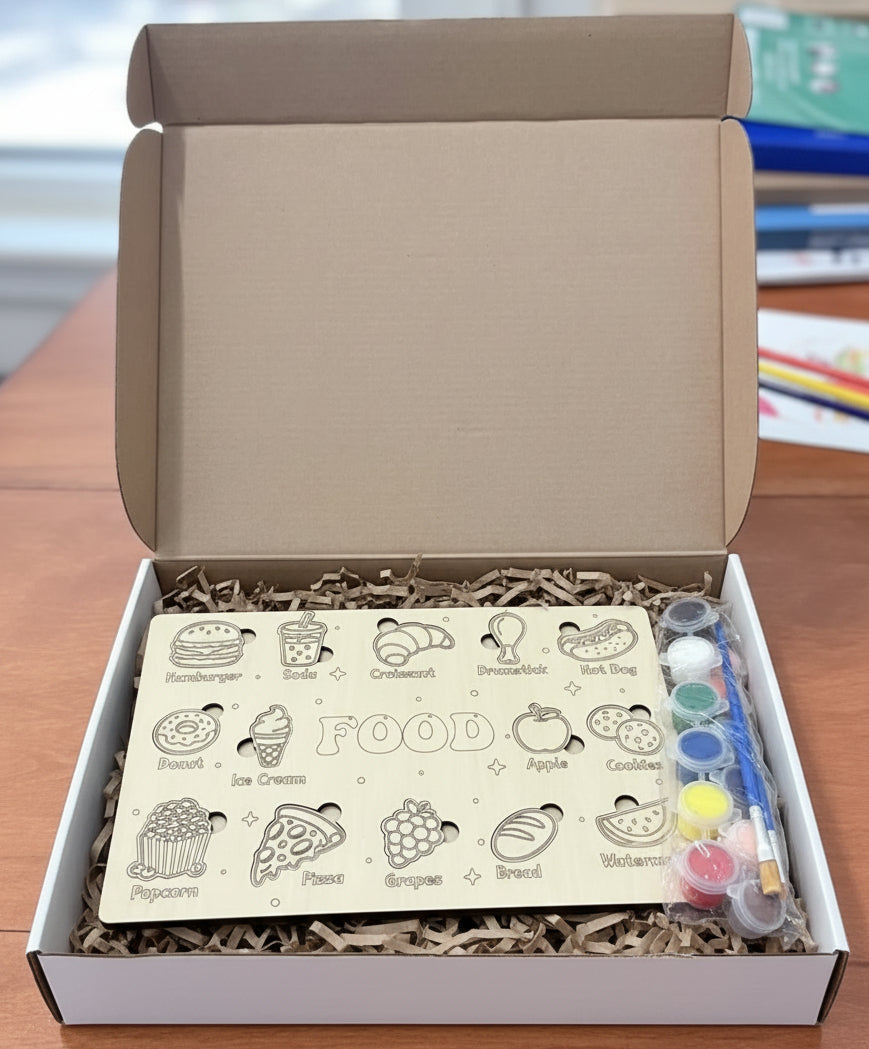 An open box containing a wooden food puzzle with shredded packing paper and a paint set with multiple colors and two brushes.
