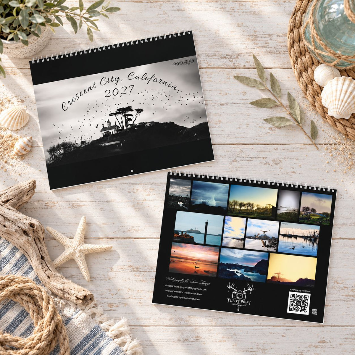 Front and back spiral-bound 2027 wall calendar  displayed on a rustic white wood surface with nautical props. The top calendar shows a black-and-white Crescent City, California, 2027 cover with a lighthouse silhouette and back shows all month pictures of Northern California Coast.