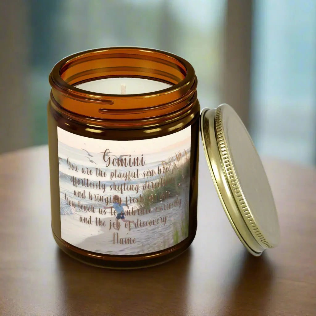 Elegant Gemini Zodiac hand-poured coconut apricot wax scented candle in a 9 oz amber glass jar with gold lid, featuring a scene of crashing waves with a man in the distance on a rock with the bright sun shining off of the waves girl running  on the beach to the ocean water and an inspirational quote personalized. A beach-inspired astrology gift, perfect for relaxation and decor.