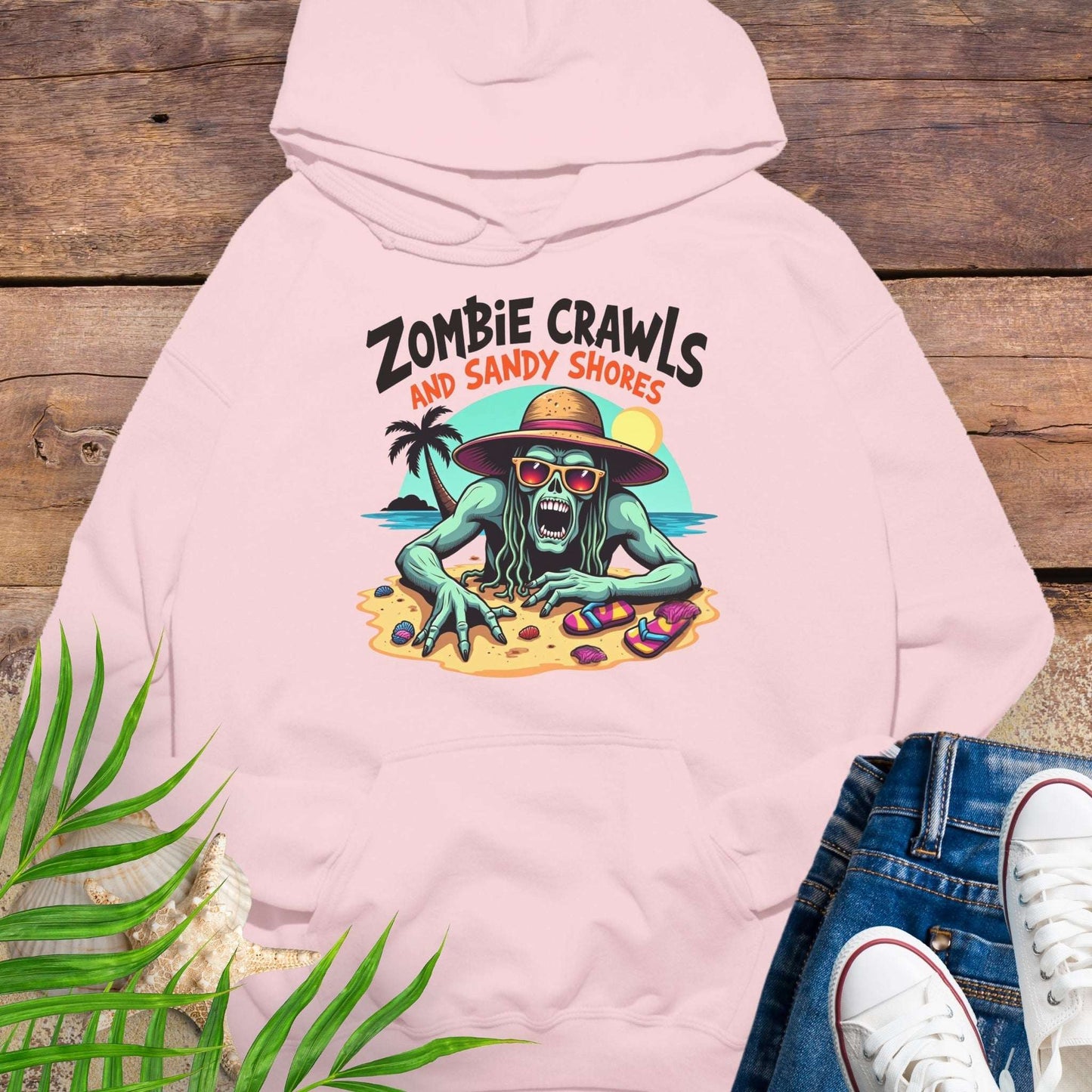Pink hoodie with zombie graphic and text 'Zombie Crawls and Sandy Shores' on a wooden surface.