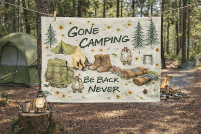 Camping-themed towel with text and illustrations hanging outdoors in a forest.