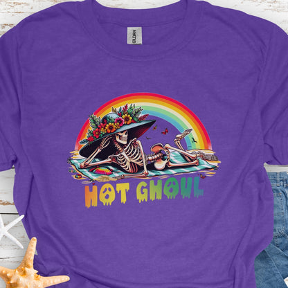 Heather Purple  t-shirt with a girl skeleton laying on beach towel with flowered hat and rainbow with rainbow dripping text that says Hot Ghoul.