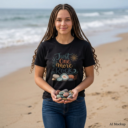 Woman wearing a black "Just One More Rock" graphic t-shirt featuring colorful beach stones and agates while holding smooth rocks on a sandy beach.