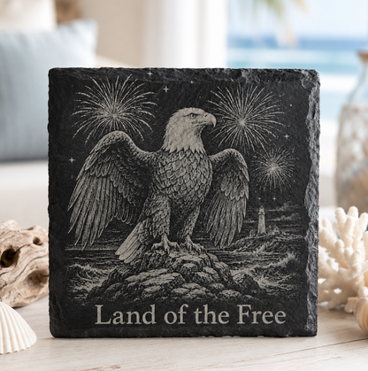 Laser engraved natural slate coaster featuring a bald eagle, fireworks, lighthouse, and "Land of the Free" with protective padded feet.