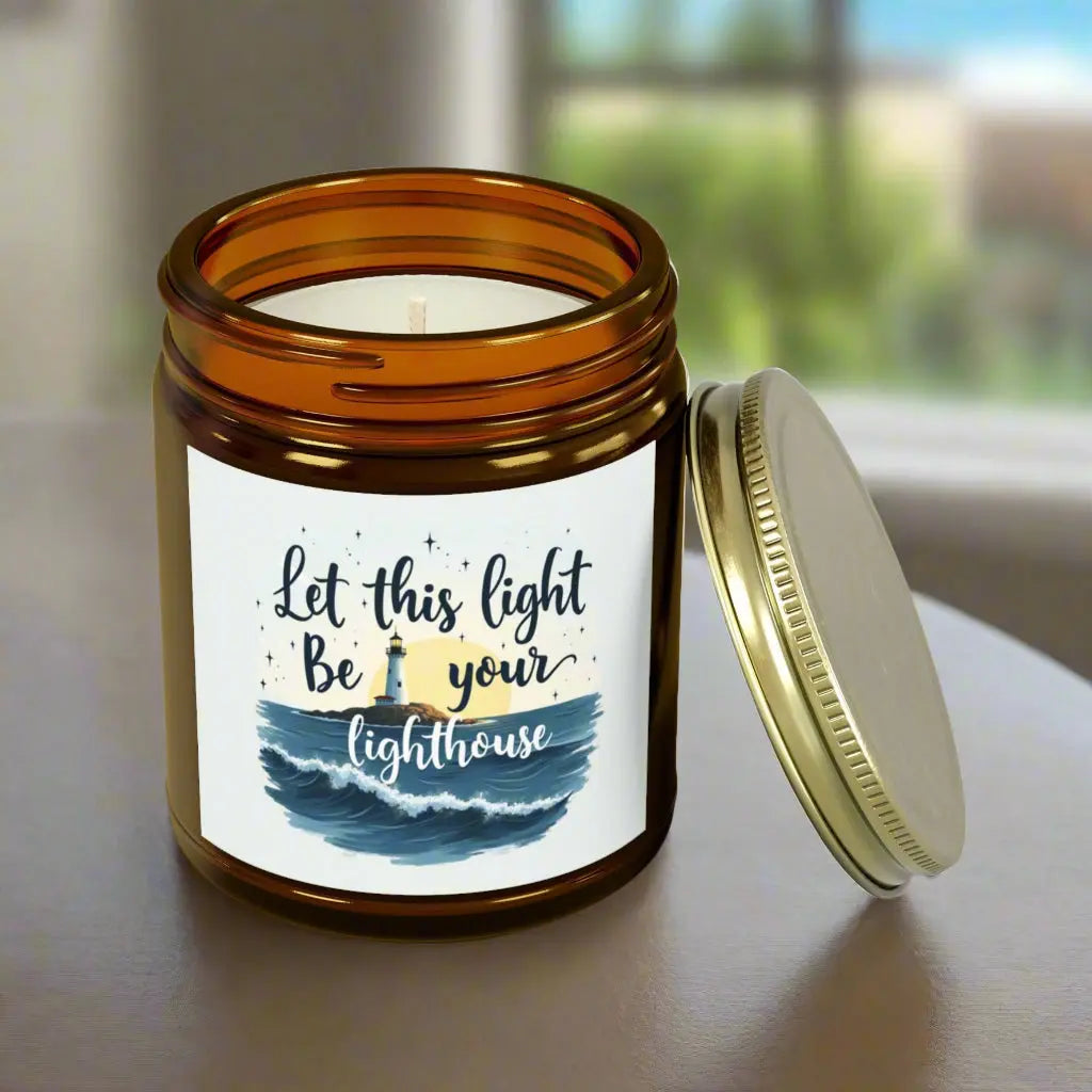 A 9 oz amber jar scented candle featuring a lighthouse with the sun and the phrase 'Let this Light Be Your Lighthouse.' A calming and inspirational candle, perfect for coastal decor.