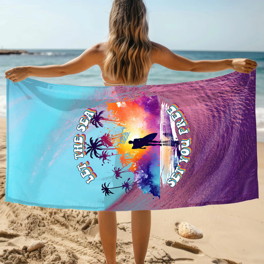 Woman holding a beach towel that has a purple wave and blue sky with the words Let the Sea Set You Free