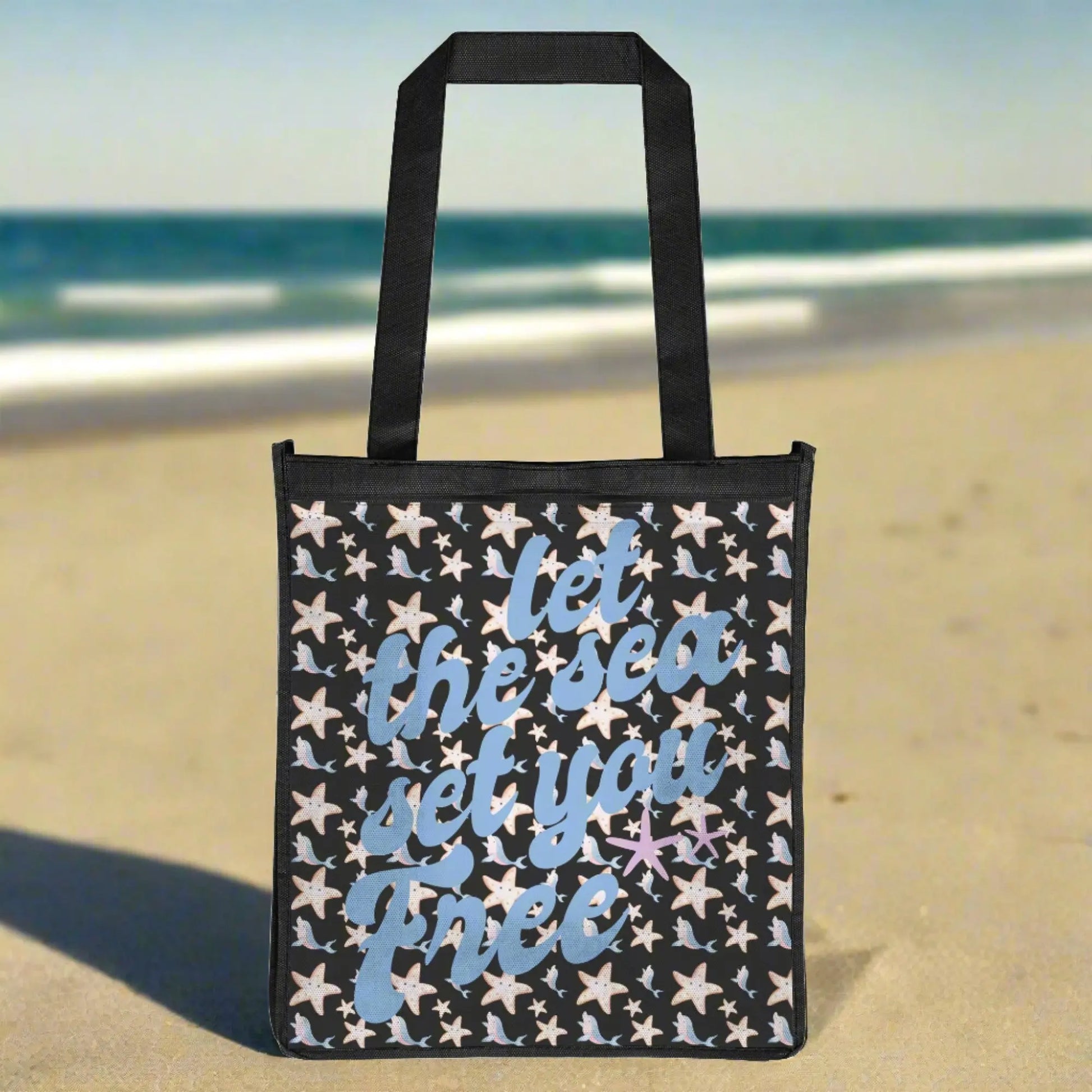 Black tote bag with cartoon star fish and dolpins in pink and blues with blue fancy text that says let the sea set you free.