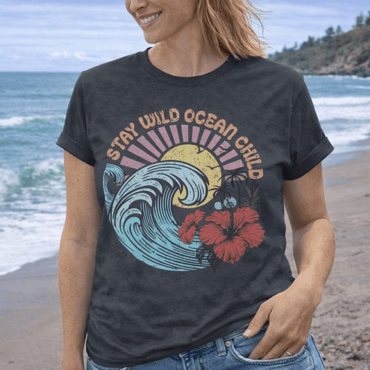 Person wearing a t-shirt with a wave and hibiscus design that says Stay Wild Ocean Child.