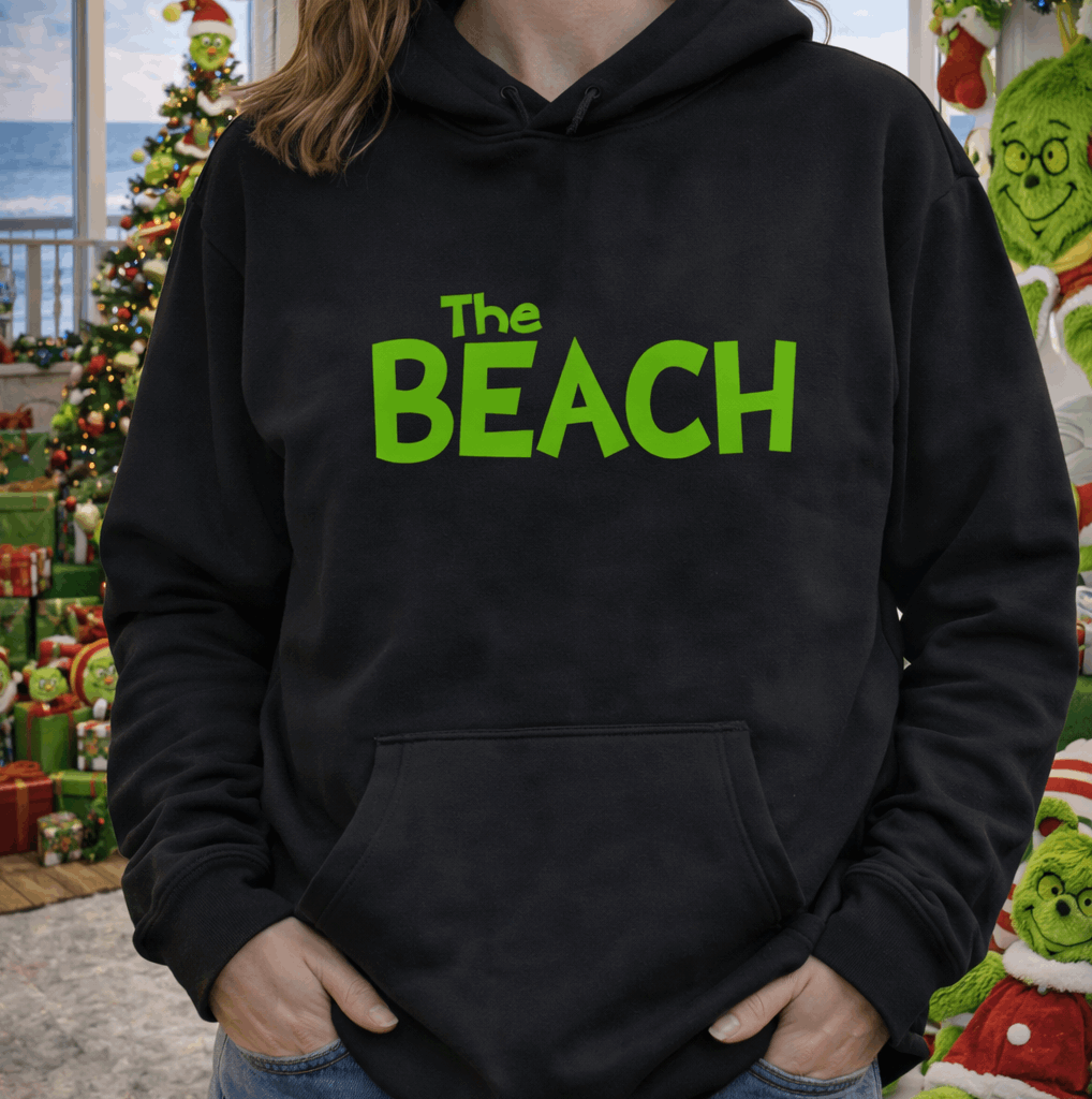 Person wearing a black hoodie with 'The Beach' in green text, standing in a Christmas Grinch decorated room.