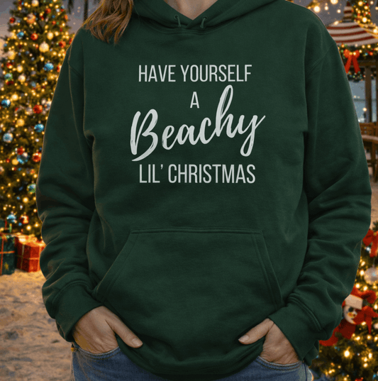 Person wearing a green hoodie with Christmas-themed text Have a Beachy lil Christmas.