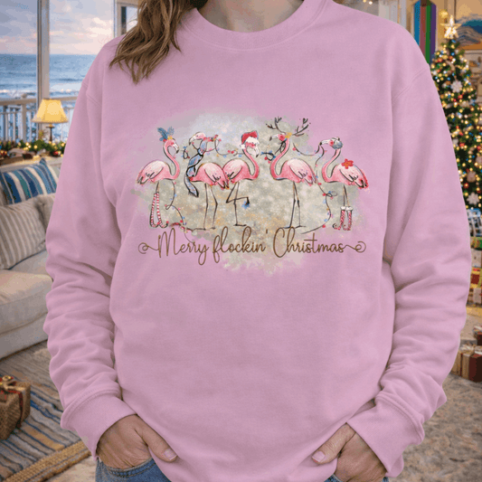 Person wearing a pink sweatshirt with flamingo design and text merry flockin’ Christmas.