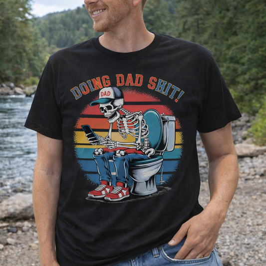 Person wearing a black t-shirt with a graphic design of a skeleton doing dad sh*t, standing by a river.