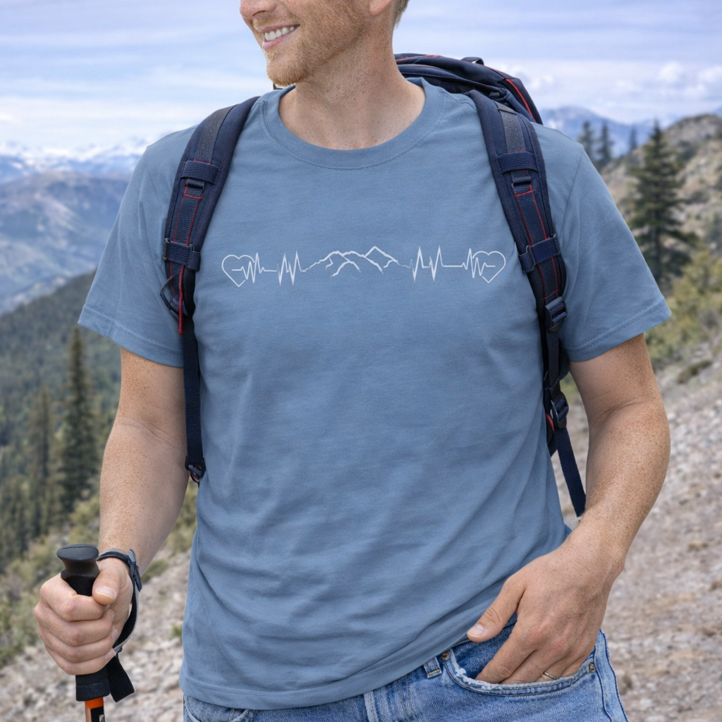 Man hiking with a scenic mountain background wearing a blue t-shirt with a heartline with a mountain design.