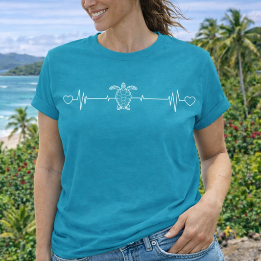 A woman wearing a turquoise blue t-shirt with ocean heartbeat design with sea turtle in center symbolizing love for sea turtles.
