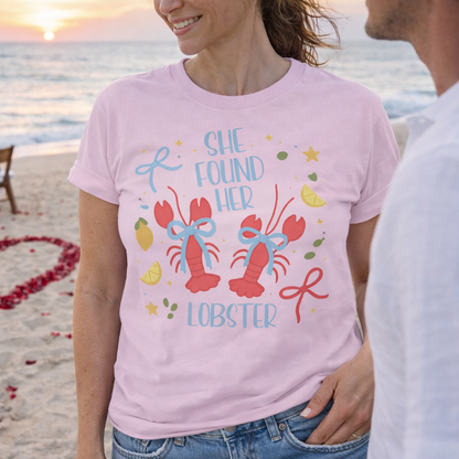 Woman wearing a pink t-shirt with 'She Found Her Lobster' design on a beach at sunset.