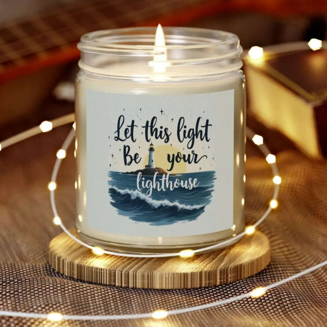 A 9 oz clear jar scented candle featuring a lighthouse with the sun and the phrase 'Let this Light Be Your Lighthouse.' A calming and inspirational candle, perfect for coastal decor.